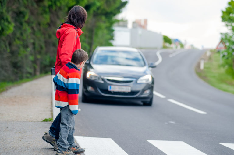 Mother and son crossing the street on the crosswalk while a car is coming