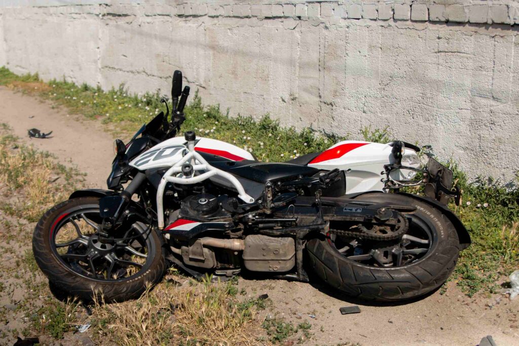 A white and red motorcycle on its side near a concrete wall after a crash involving Florida road rash injuries.