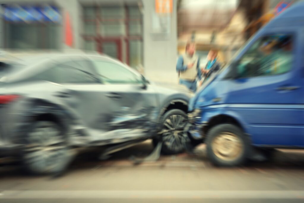 Blurred view of a collision between a grey sedan and a blue van on a city street.