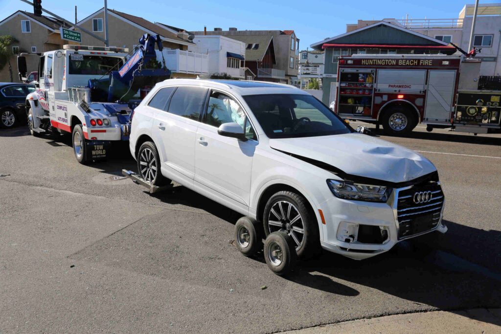 White damaged SUV hitched to a tow truck beside a parked fire engine.
