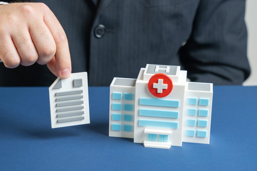 Hand placing a document next to a miniature toy hospital on a desk.