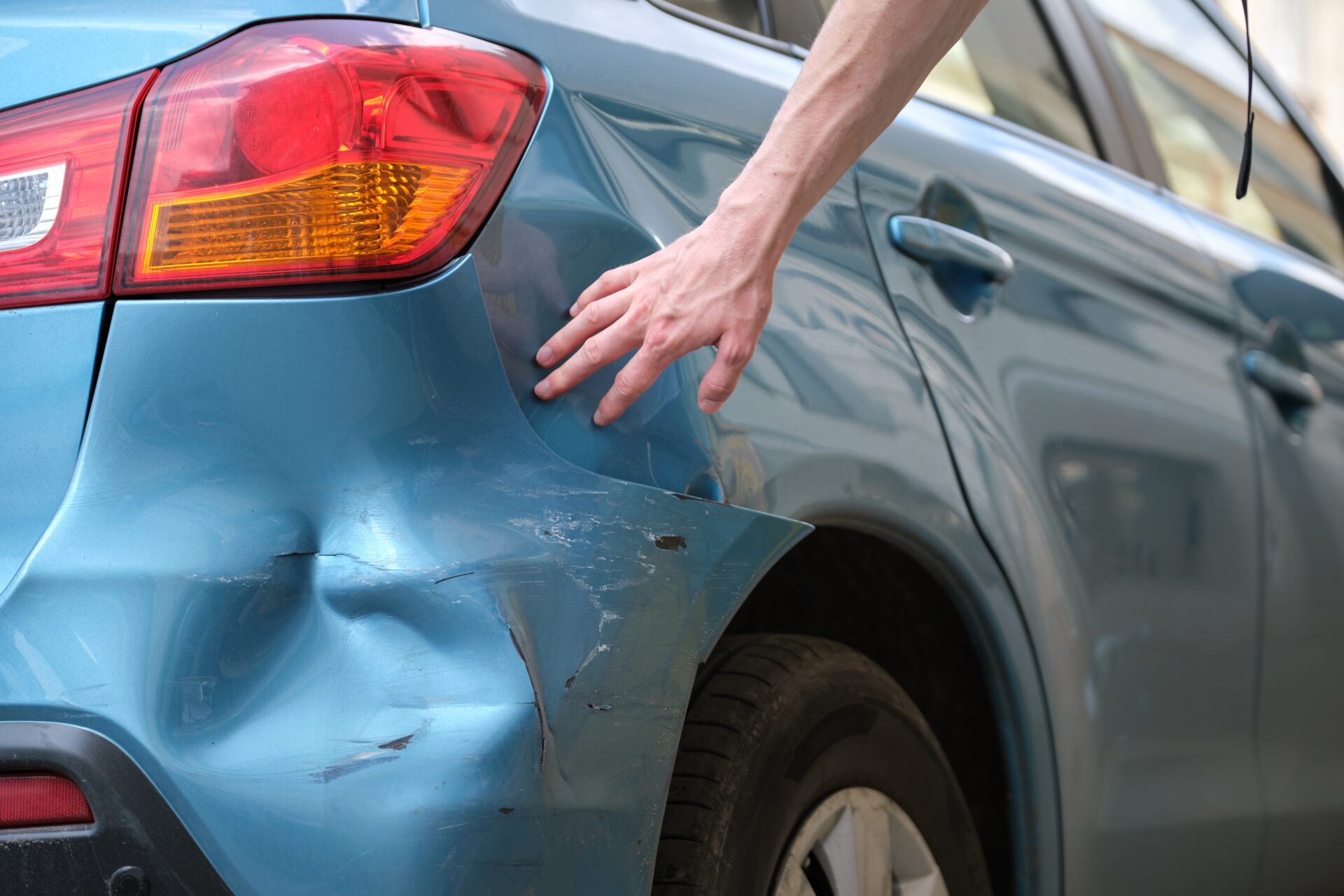 A driver's hand investigating damage to their vehicle after a hit-and-run car accident.