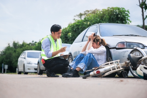 Police officer assisting injured cyclist after car accident with bicycle on roadside