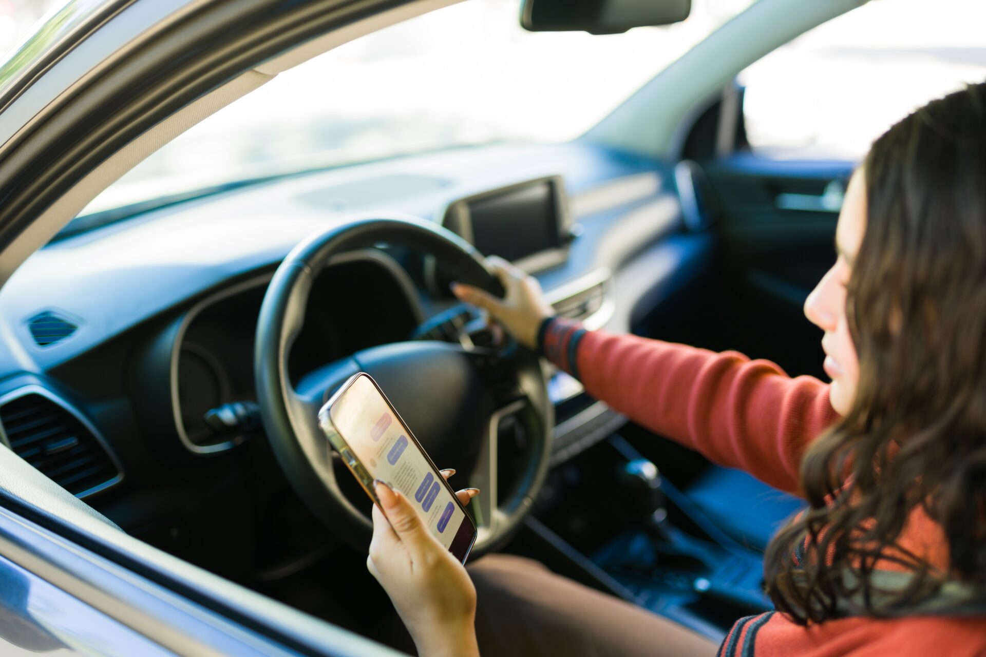 A female driver being distracted by using their cell phone, texting and driving at the same time.