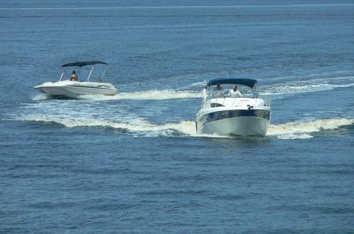 Two motorboats creating wakes while cruising side by side on open water.