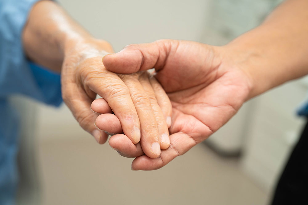 Caregiver holding an elderly woman’s hands representing resident safety, care, and concerns about neglect or abuse