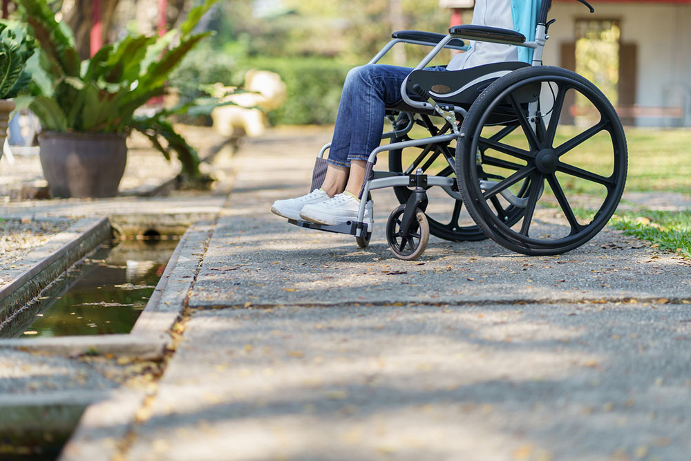 Woman sitting in a wheelchair on an outdoor path during recovery