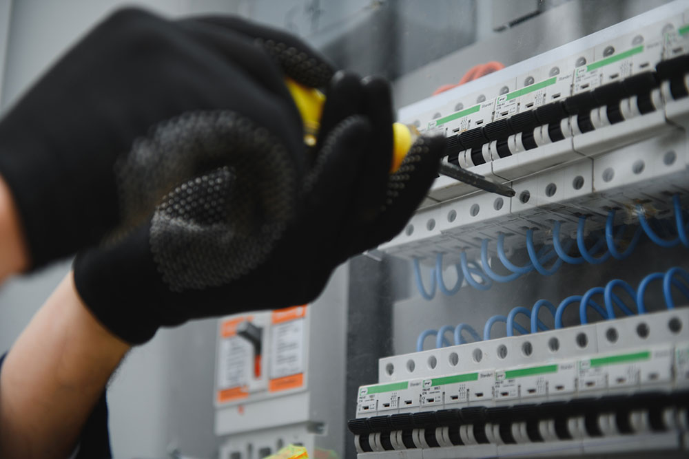 Electrician adjusting circuit breakers in a control panel representing electrical safety and maintenance duties