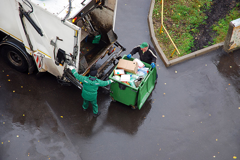 Garbage collection workers loading a garbage truck in a residential area representing heavy vehicle accident risks