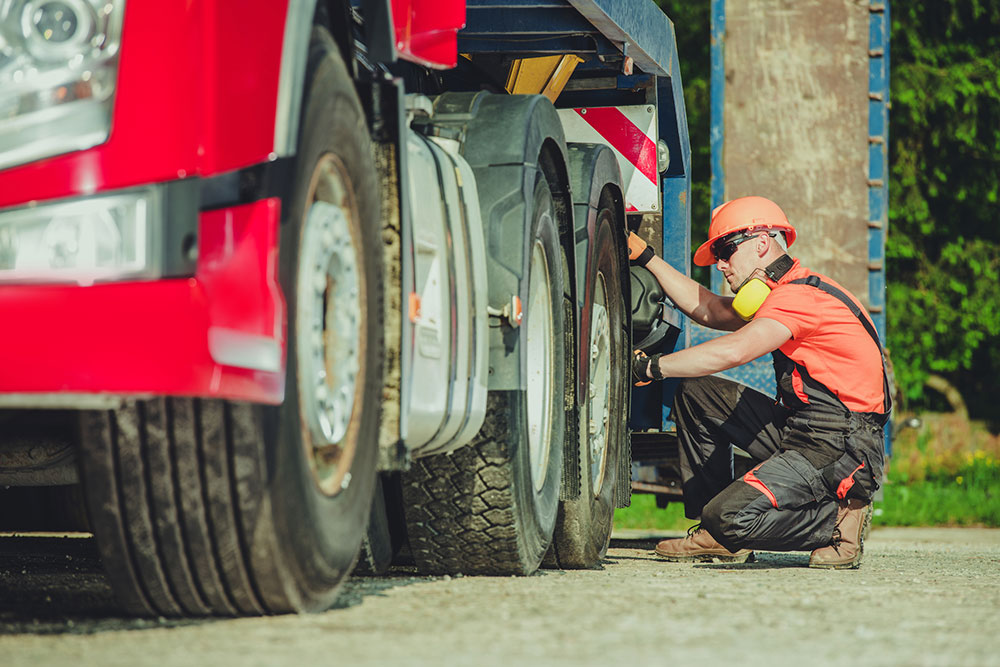 Worker inspecting truck tires representing maintenance issues and safety compliance in heavy vehicle cases