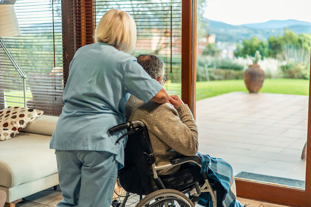 Nurse comforting an elderly patient in a wheelchair while looking outside