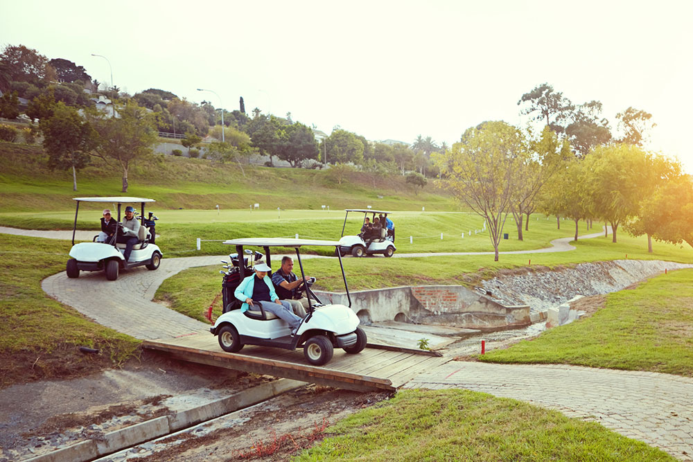 Group riding in a golf cart on a golf course path near a water hazard