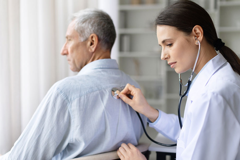 Female doctor examining a senior man’s back with a stethoscope during a medical checkup
