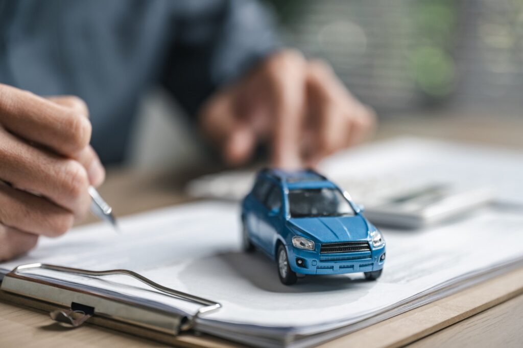 A person writing policy details next to a toy car when car insurance rates go up after an accident in Florida.