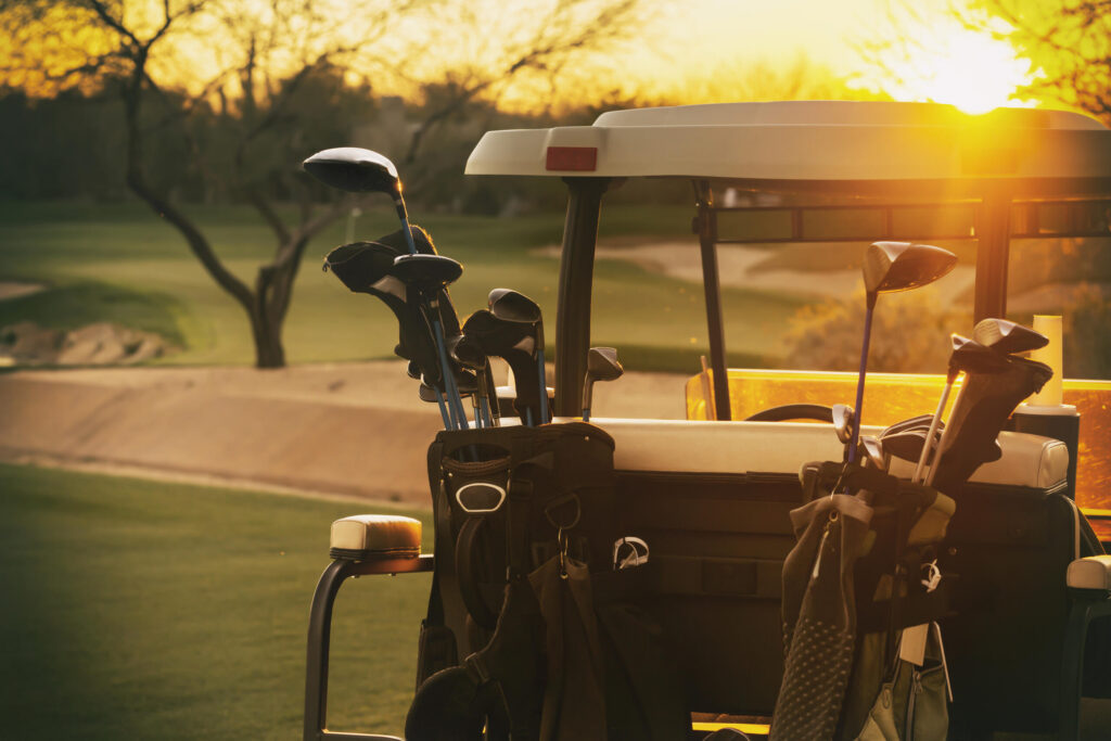 Golf cart loaded with clubs parked on a course during sunset.