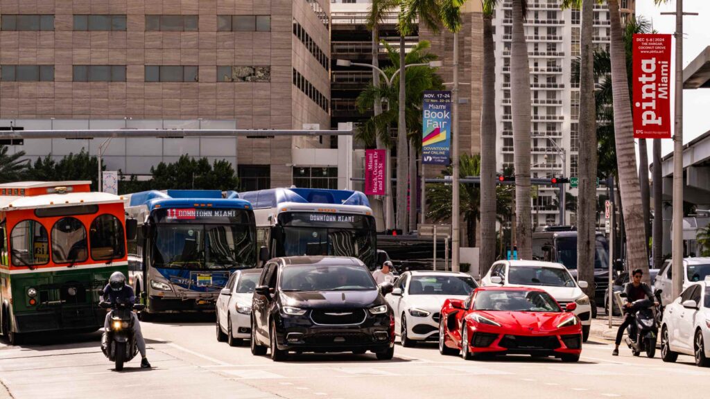 Motorcyclists riding through a crowded Florida intersection with buses and cars, where Roman Austin helps riders fight insurance bias after a crash.