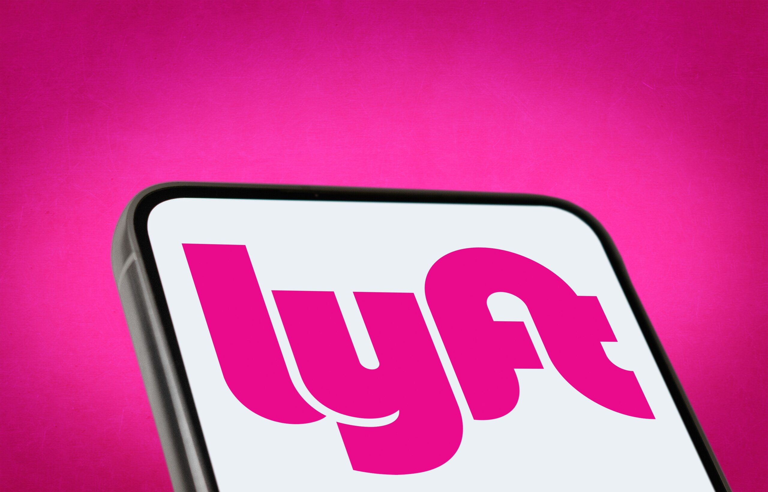 Close-up of a smartphone screen displaying the pink and white Lyft rideshare service logo against a solid pink background.