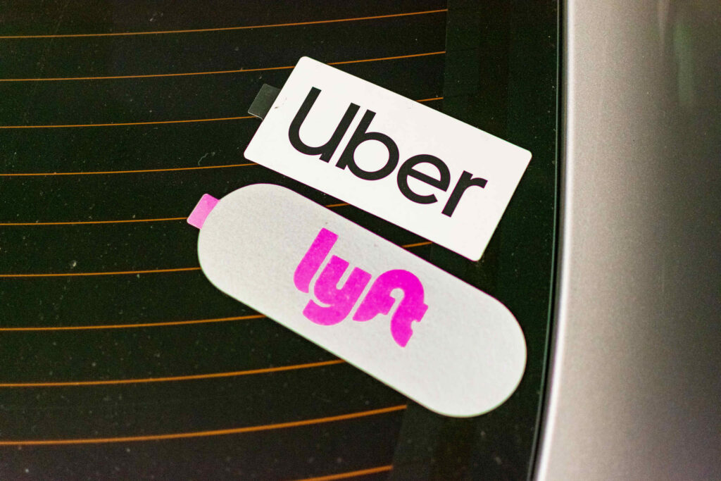 Close-up of Uber and Lyft rideshare service logo stickers displayed on the glass window of a vehicle.