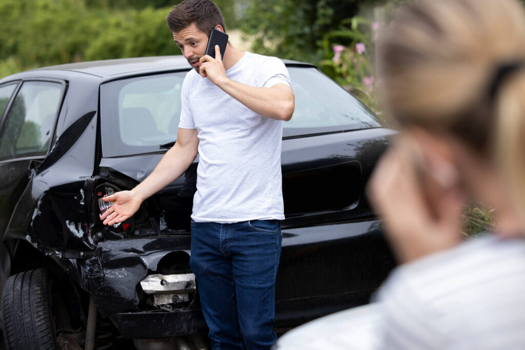 A stressed driver talking on a smartphone next to a crashed vehicle highlights How St. Petersburg Attorneys Obtain Cell Phone Records to Prove Distracted Driving.