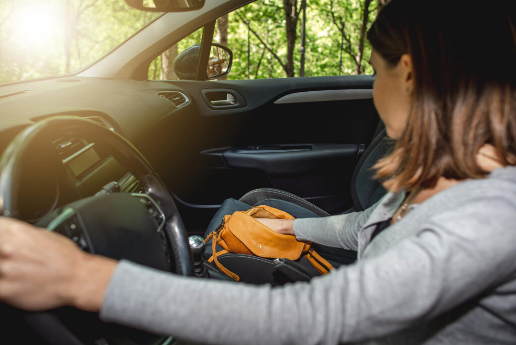 A woman reaching into her handbag while steering a car demonstrates visual distractions linked to Distracted Driving Statistics in Florida and Safety Harbor.