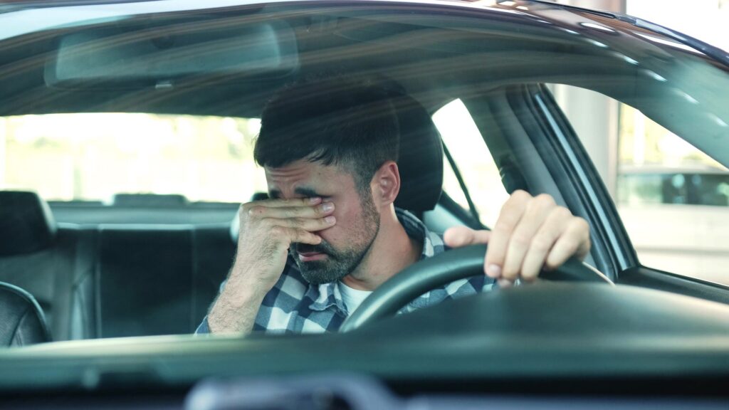 An exhausted man rubbing his eyes behind the wheel illustrates the dangers of Fatigued Lyft Drivers in Safety Harbor.