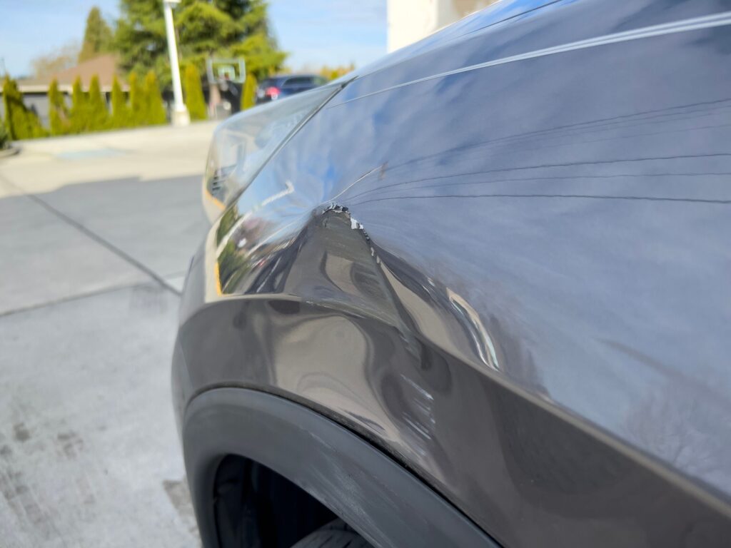 A distressed man examining damage on his white car following a crash related to Florida hit and run criminal penalties.