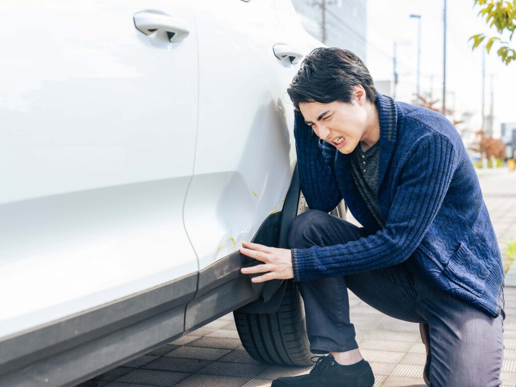 Frustrated driver inspecting side door damage on a vehicle subject to Florida hit and run criminal penalties.