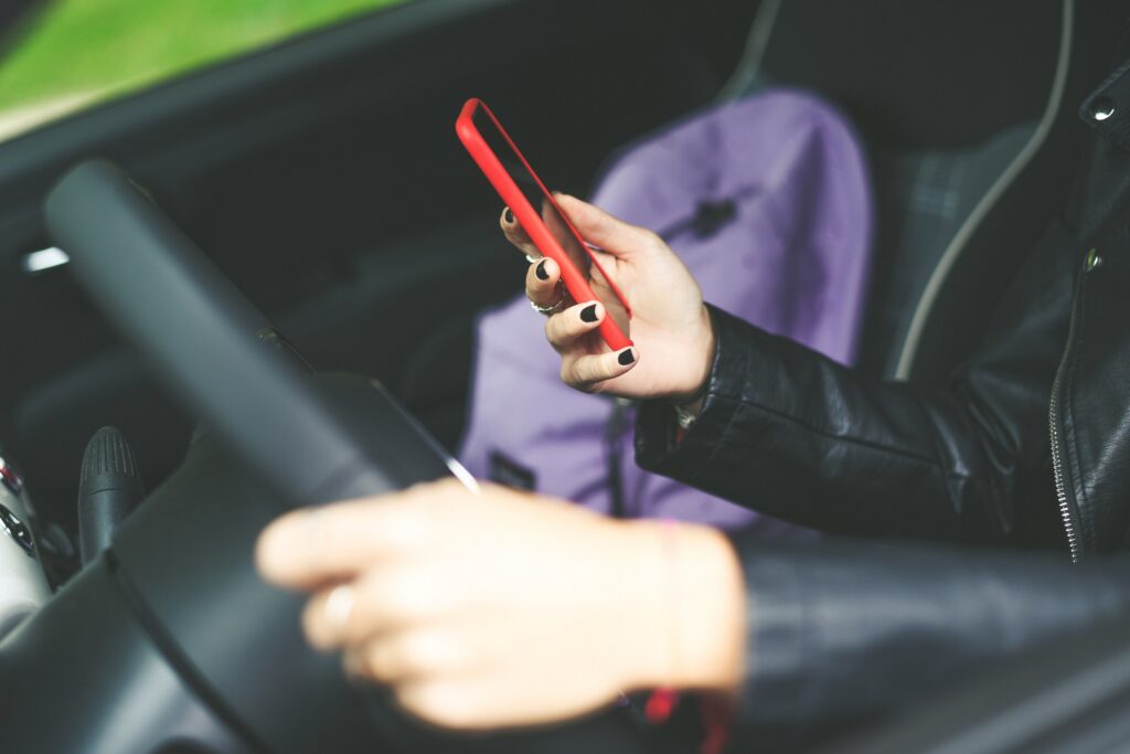 Driver holding a red smartphone while keeping one hand on the steering wheel.