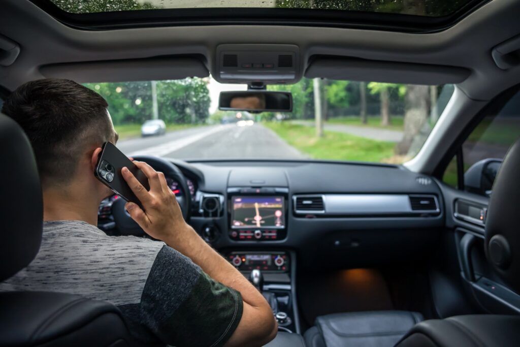 Man holding a smartphone to his ear while driving a car down the road.