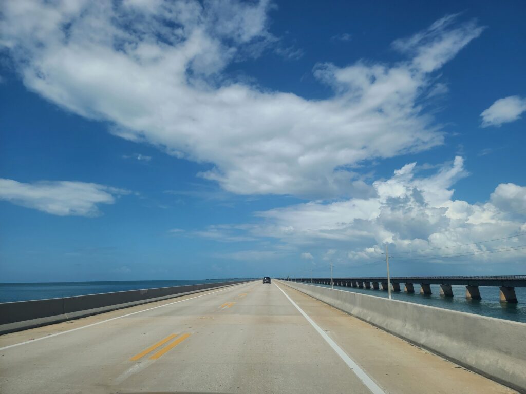 Long open highway bridge stretching over blue ocean water under a partly cloudy sky.