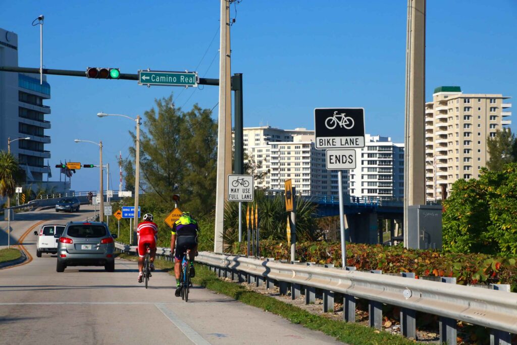 Two cyclists riding along a coastal road near a bike lane ends sign.