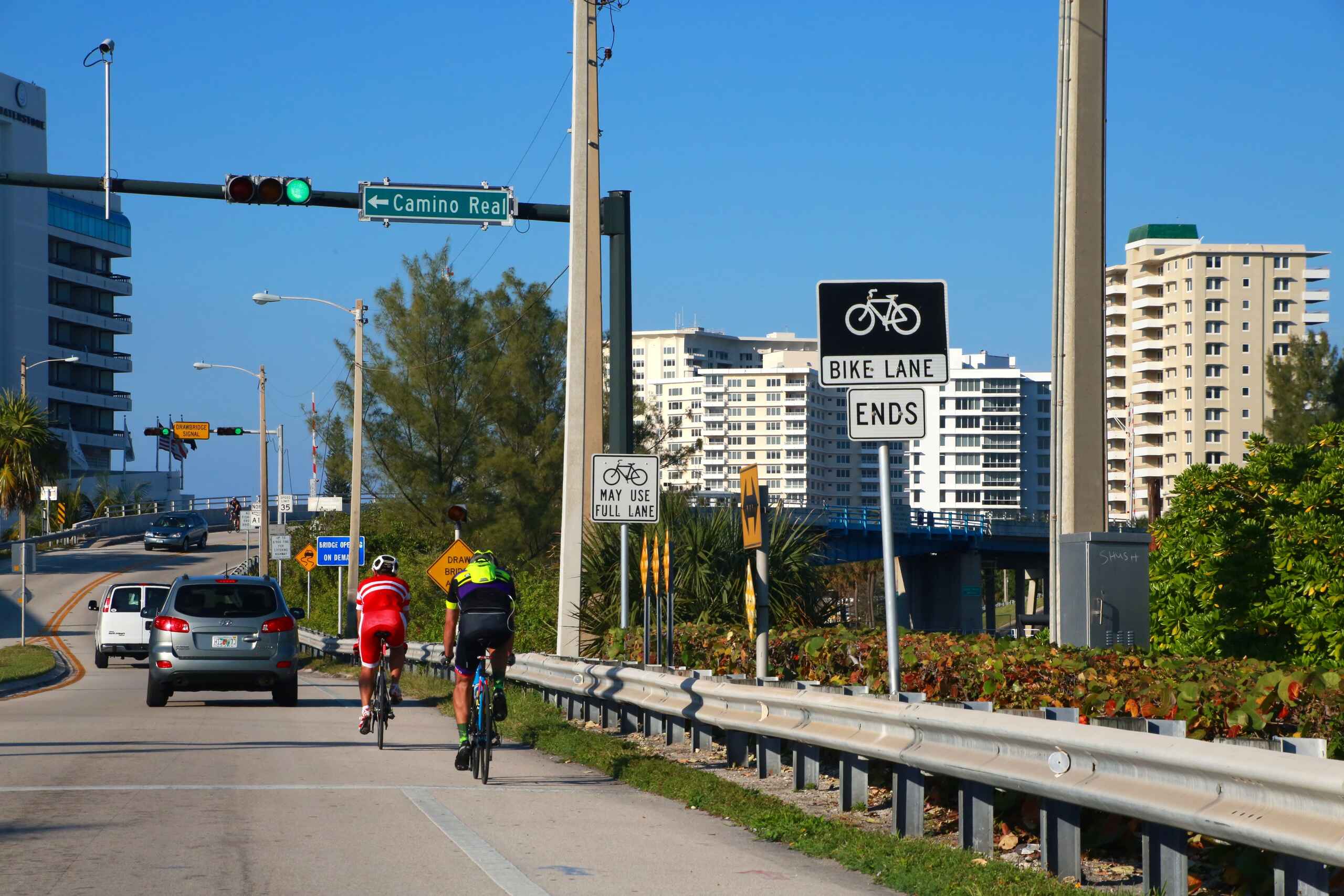 Two cyclists riding along a coastal road near a bike lane ends sign.