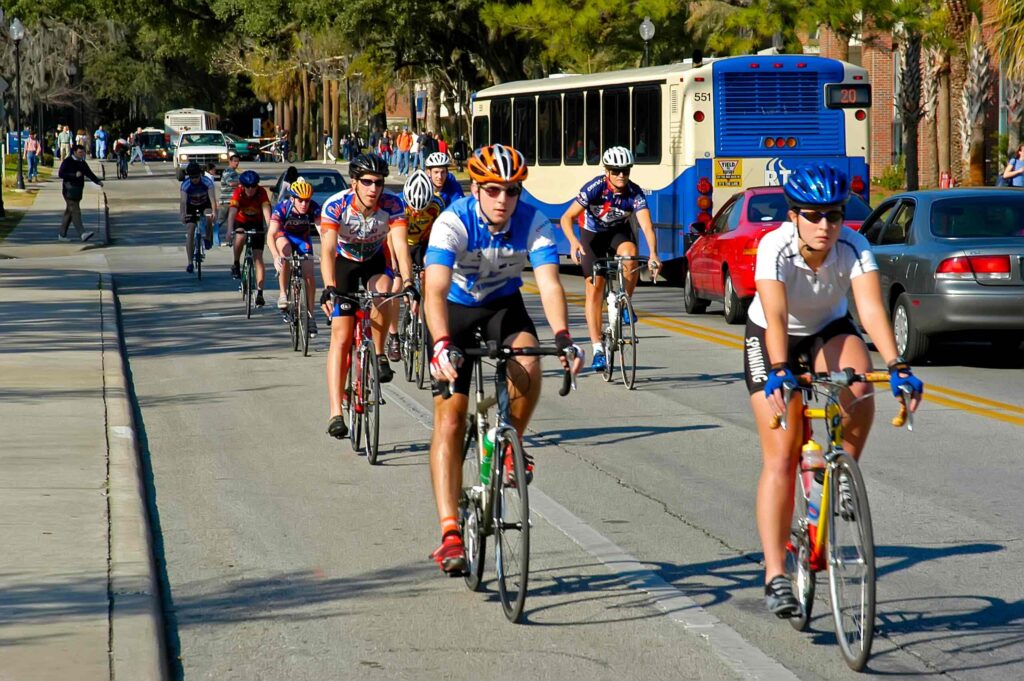 Group of cyclists wearing helmets riding together on a city street beside traffic.